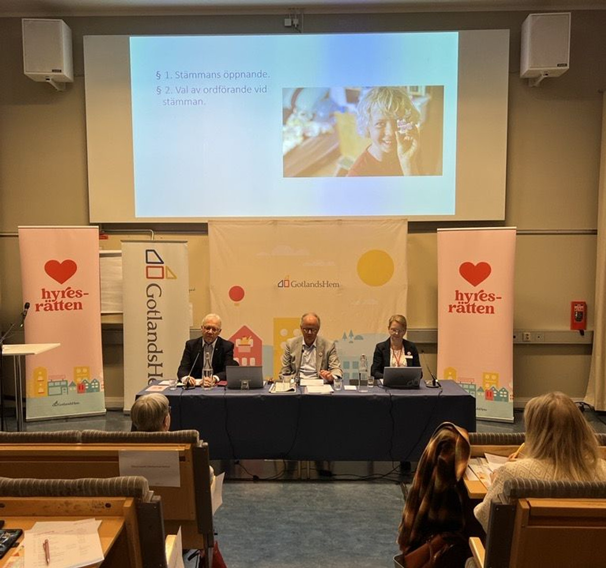 Bo Björkman, avgående vice ordförande, Peter Norman, avgående styrelseordförande och Helena Olofsson, vice vd på GotlandsHem sitter vid ett bord framför en stor skärm.