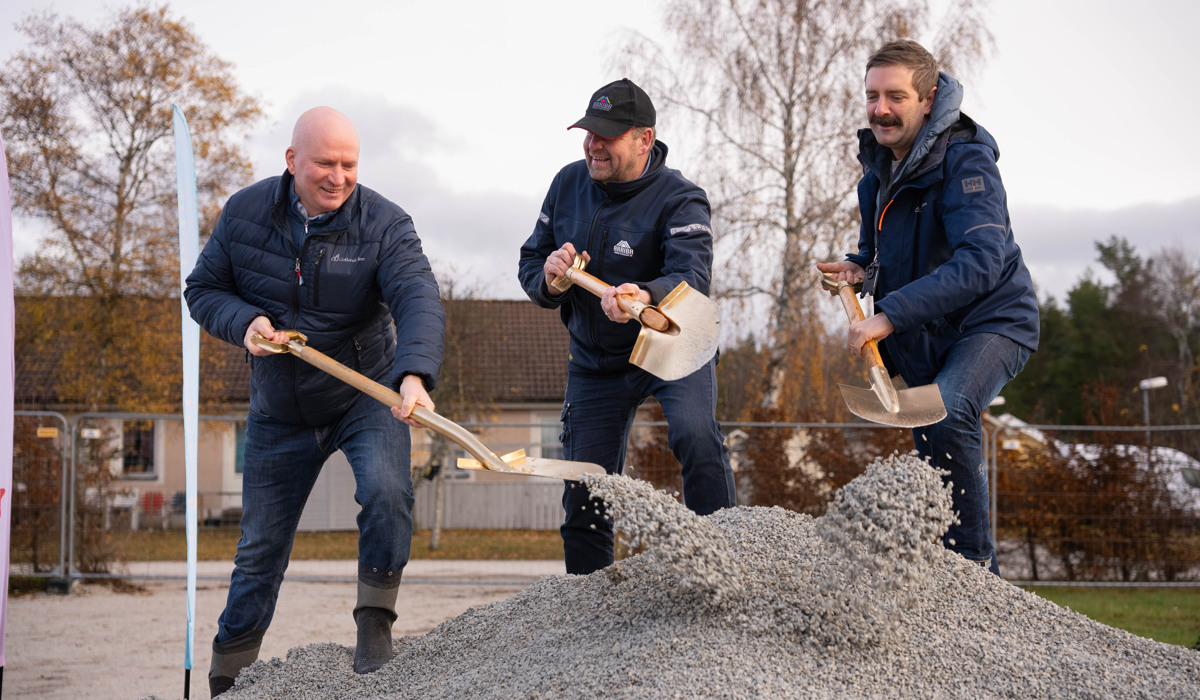 Tre män i blåa kläder gräver i en grushög med varsin guldspade.