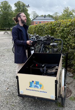 En man som står vid en lådcykel och håller en hjälm i händerna.