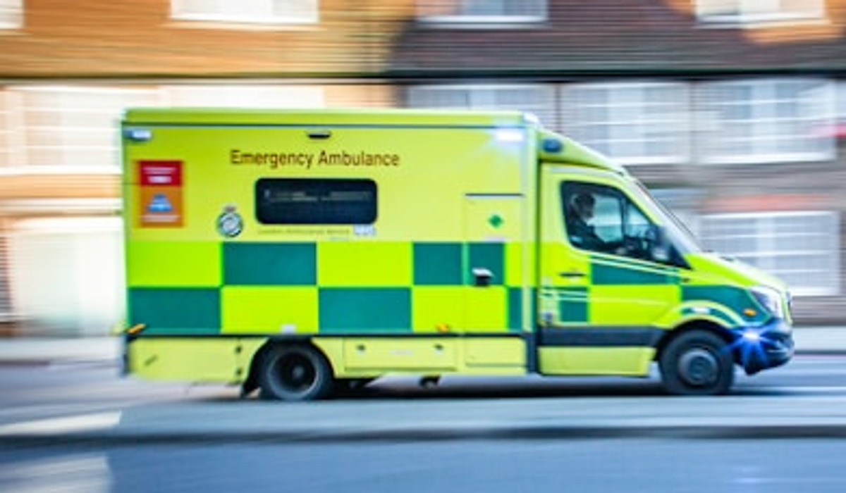 En gul ambulans kör längs en gata bredvid höga byggnader.