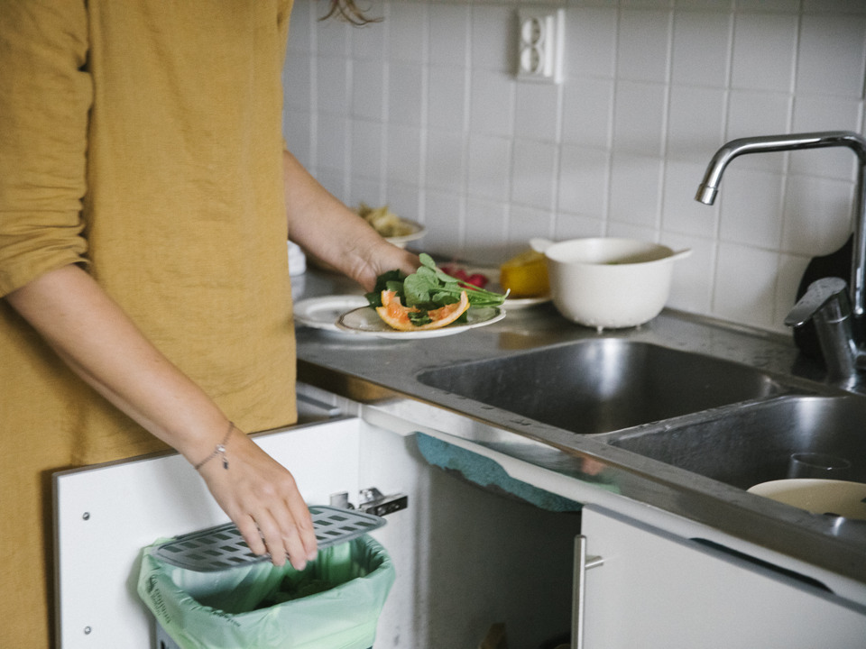 En person slänger matrester i en kompost under diskbänken.