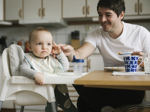 En bebis och en pappa vid matbordet.