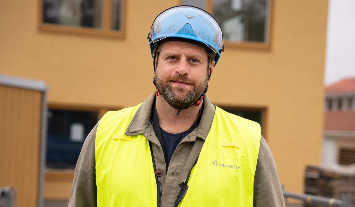 Projektledare Stefan Pettersson står framför en av bostäderna som håller på att byggas på Silvergatan i Hemse. Han har bygghjälm och reflexväst. Stefan är runt 35-40 år, han ler vänligt, har gråbrunt skägg och en grön skjorta under reflexvästen. 