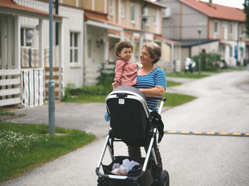 Kvinna med flicka i famnen drar en barnvagn.