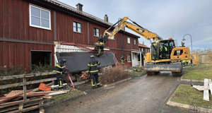 Rött trähus i två våningar rivs av en stor gul grävmaskin.