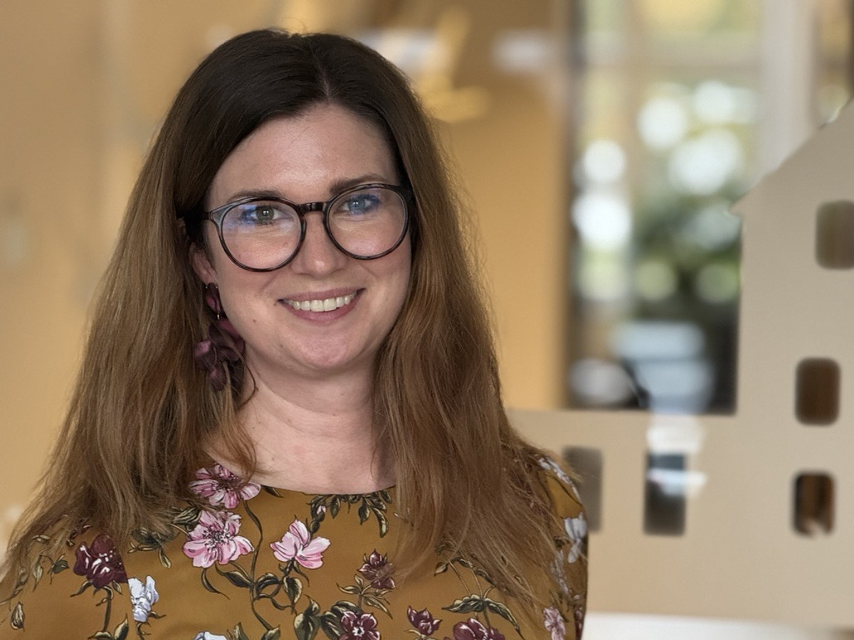 En kvinna med brunt, halvlångt hår och blommig blus ser in i kameran