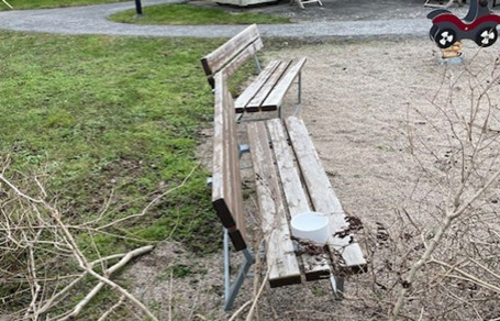 Två slitna bänkar i trä, en avklippt gren i förgrunden.