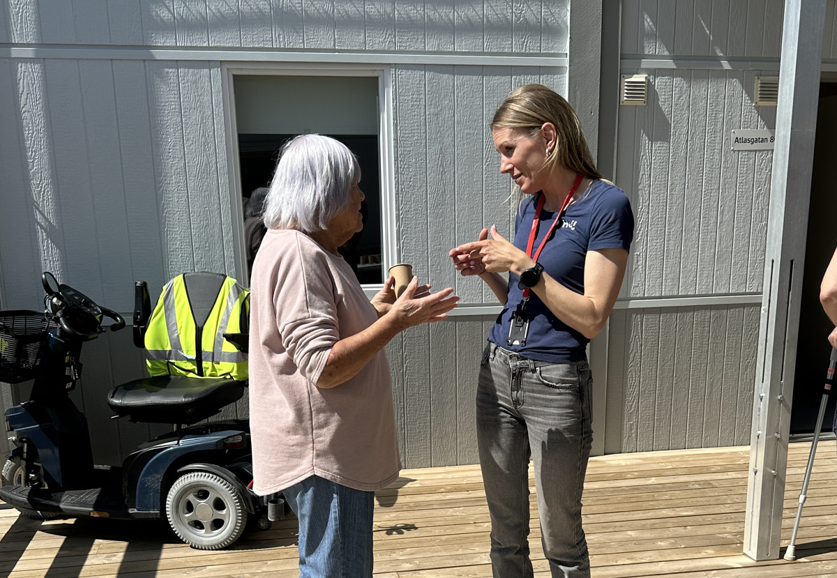 En medarbetare på GotlandsHem står och pratar med en äldre kvinna. Solen skiner och det är sommar.