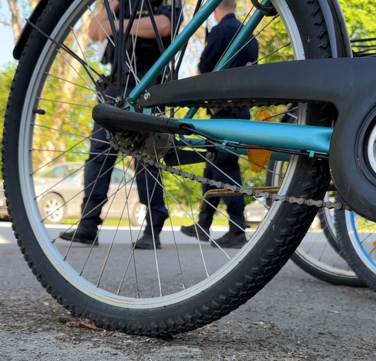 En närbild av ett cykeldäck på marken. Bakom går två poliser