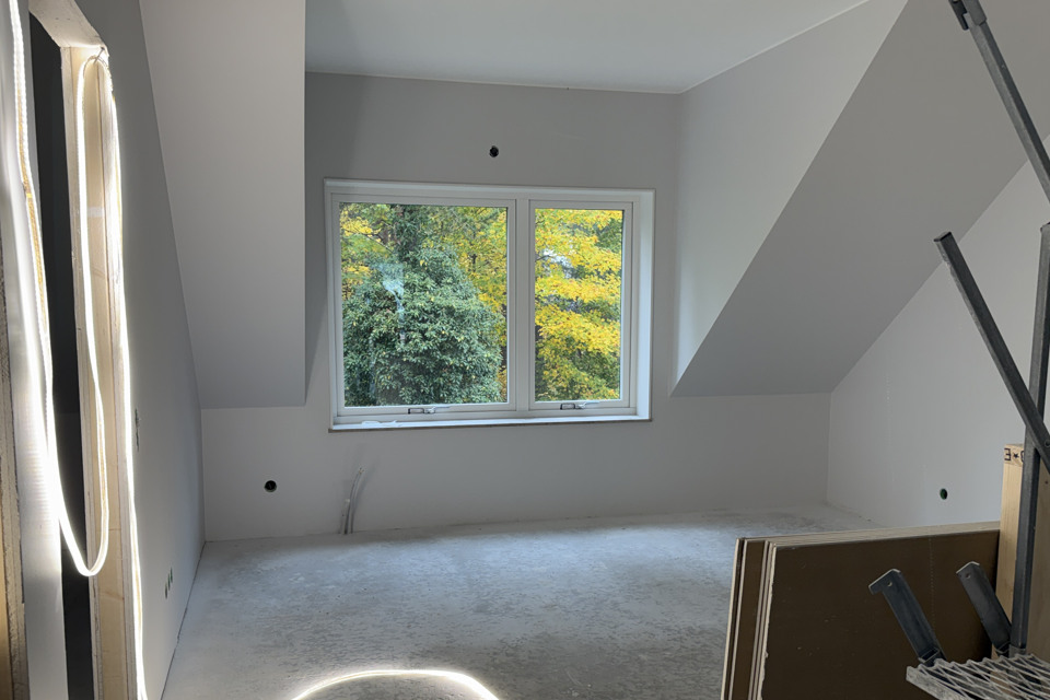 Ett tomt rum i e nybyggd bostad. Ett fönster ut om höstfärgade löv. Till höger en trappa upp till rummet.